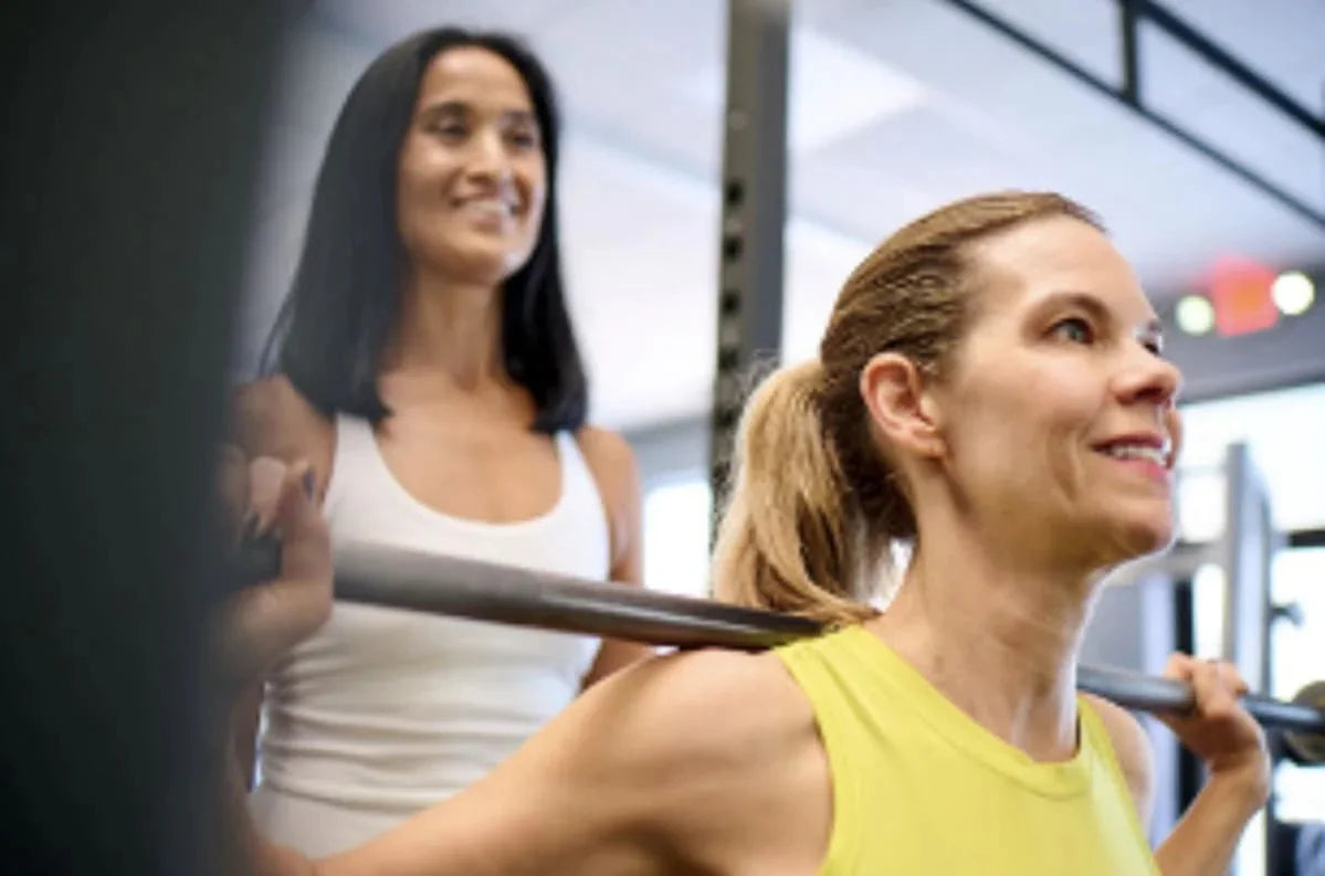 Two women strength training together in a gym
